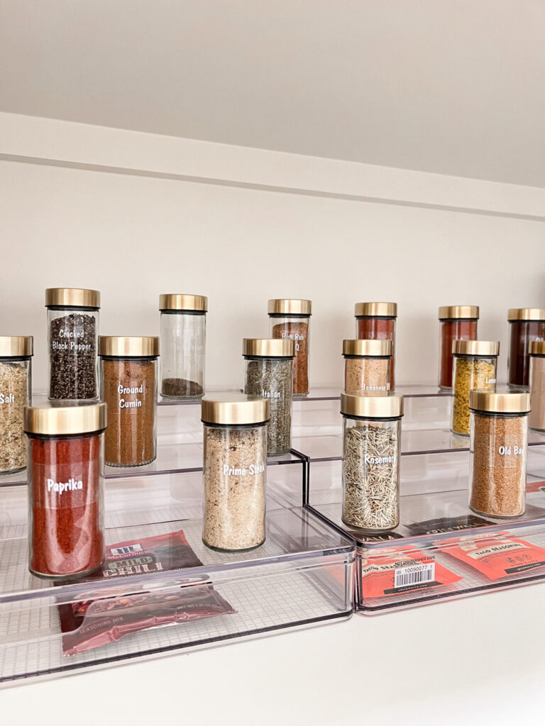 Three-tier acrylic organizer riser, organizing spices in glass jars with gold lids and custom labels. 