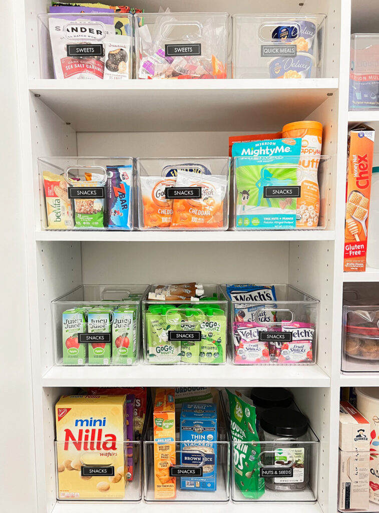 Pantry shelves full of snacks, organized into clear acrylic bins from The Container Store. 
