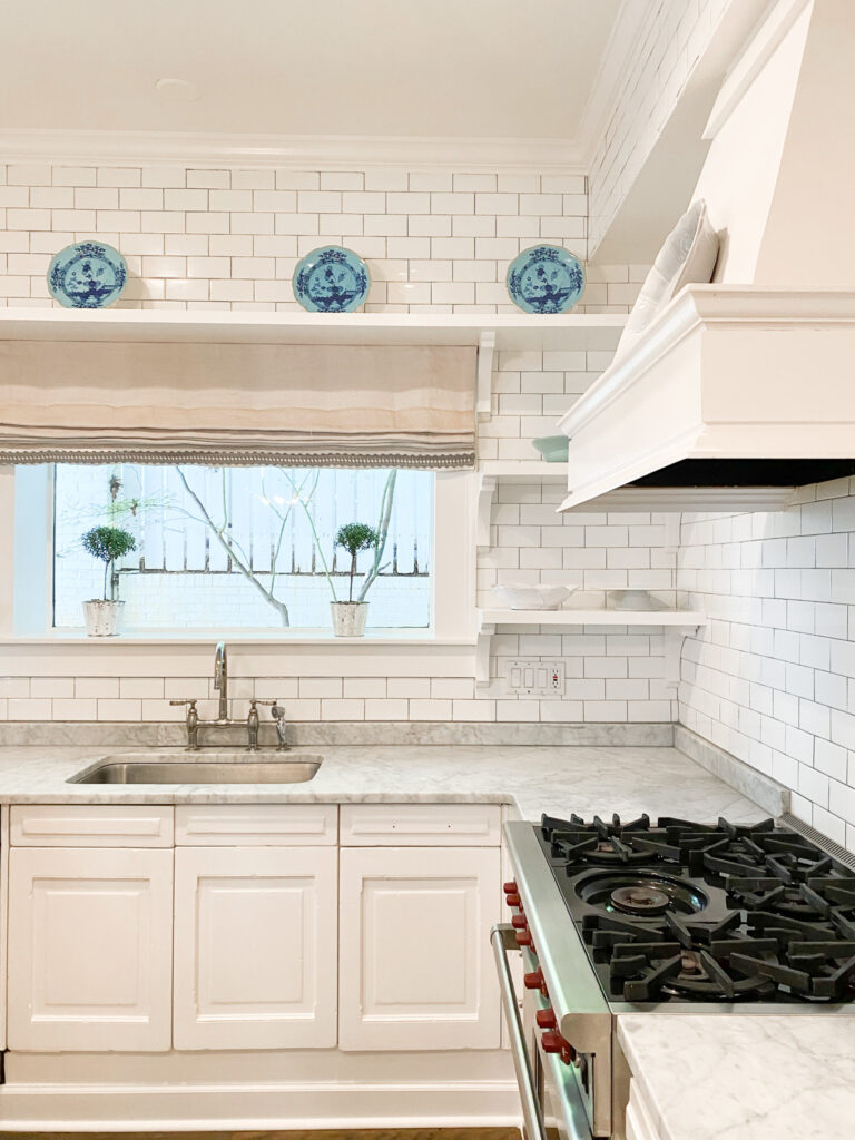 A luxury kitchen with gray marble countertops, white shaker cabinets, subway tile, a white range hood, and a window above the sink. How to avoid impulse buying