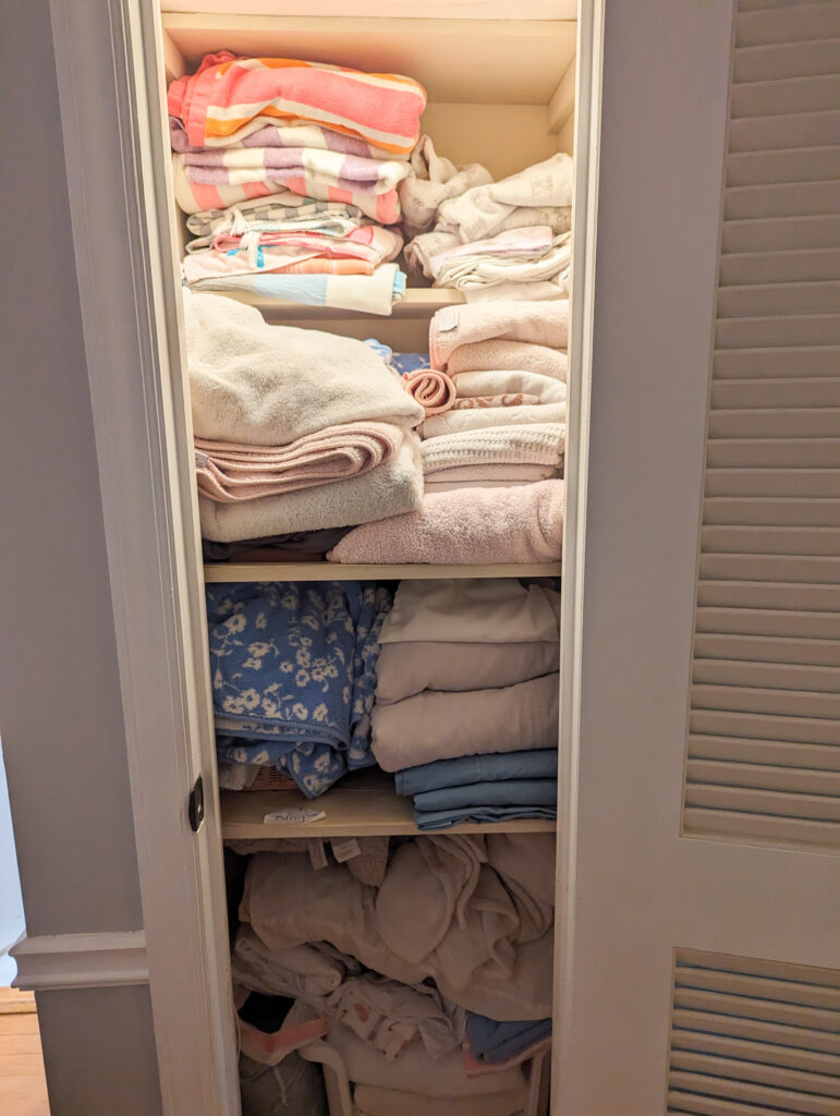 A disorganized, cluttered linen closet that is messy and stuffed with linens due to impulsive buying.